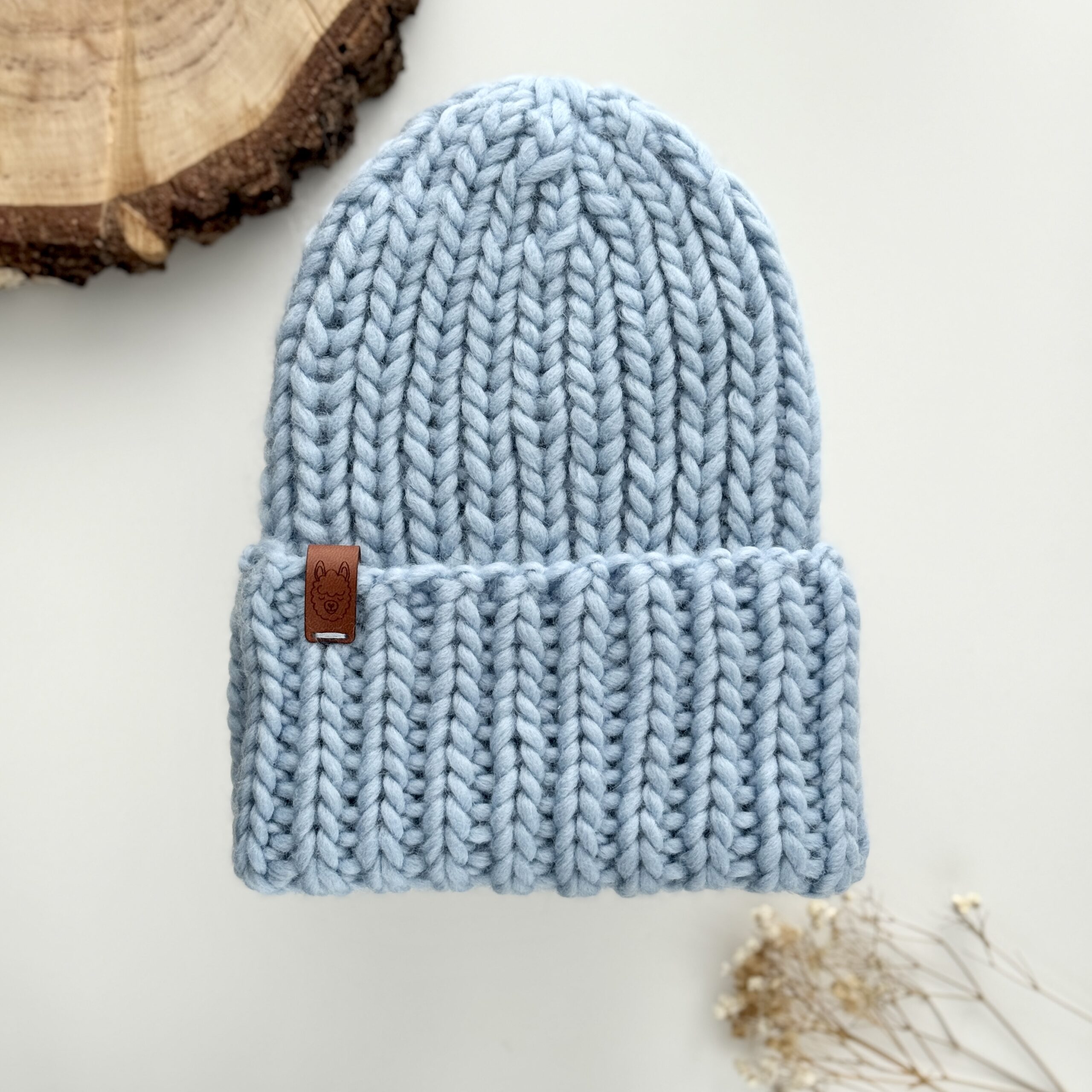 Czapka z wełny w kolorze błękitnym, zrobiona na drutach ściegiem ściągaczowym.