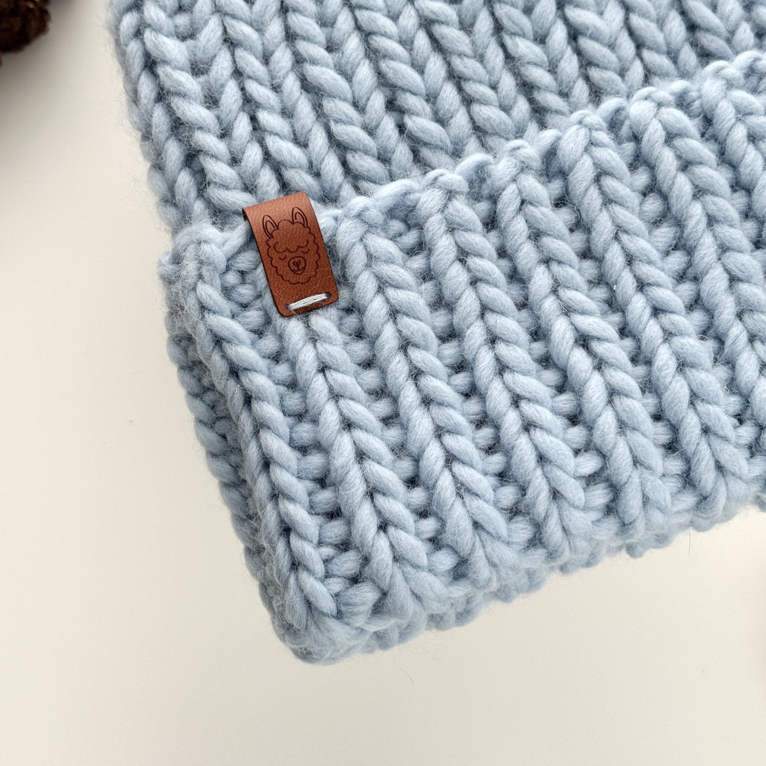 Czapka wełniana w kolorze jasny niebieski w zbliżeniu, z widocznym ściegiem ściągaczowym i metką.