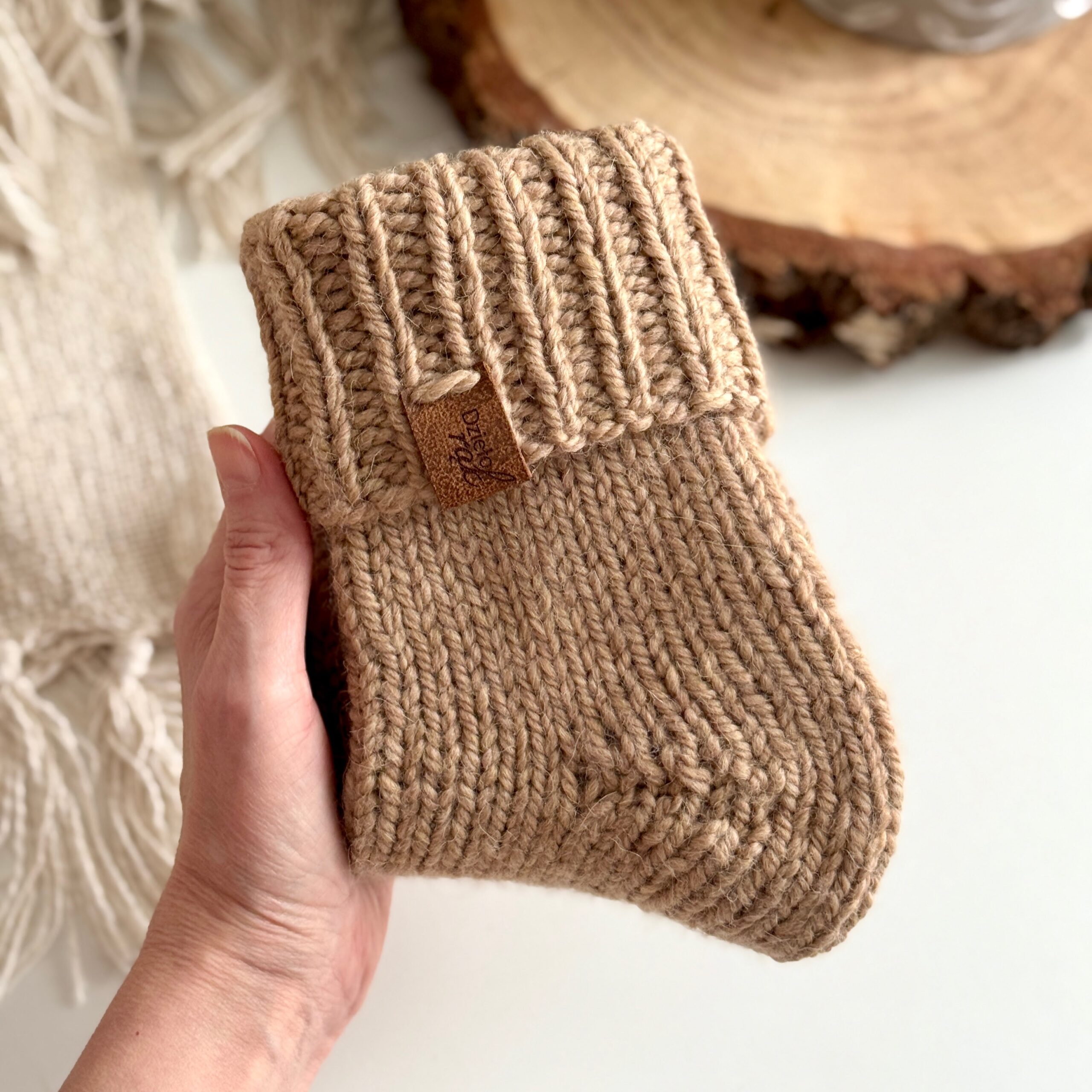 ręcznie dziergane skarpety w kolorze beżowym trzymane w dłoni.