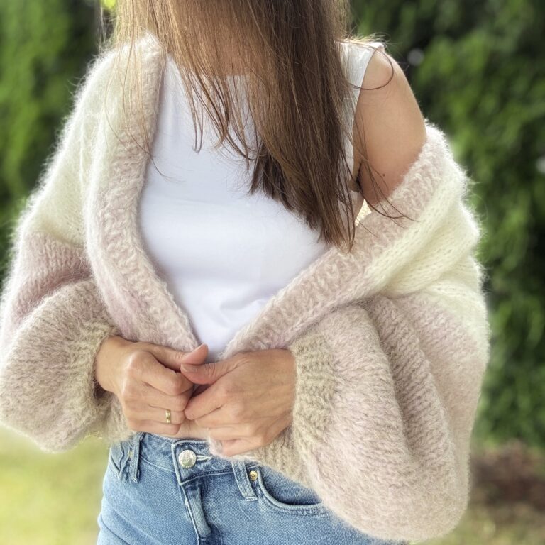 Ręcznie robiony kardigan z alpaki Różana Mgła na kobiecej sylwetce. Puszysty sweter oversize w odcieniach kremu, pudrowego różu i beżu z szerokimi rękawami.