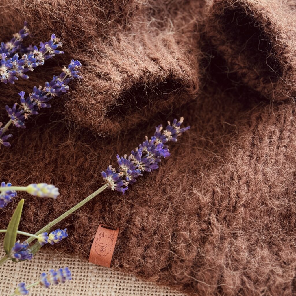 Sweter z wełny alpaki ręcznie dziergany w przybliżeniu, z metką i kwiatem lawendy.