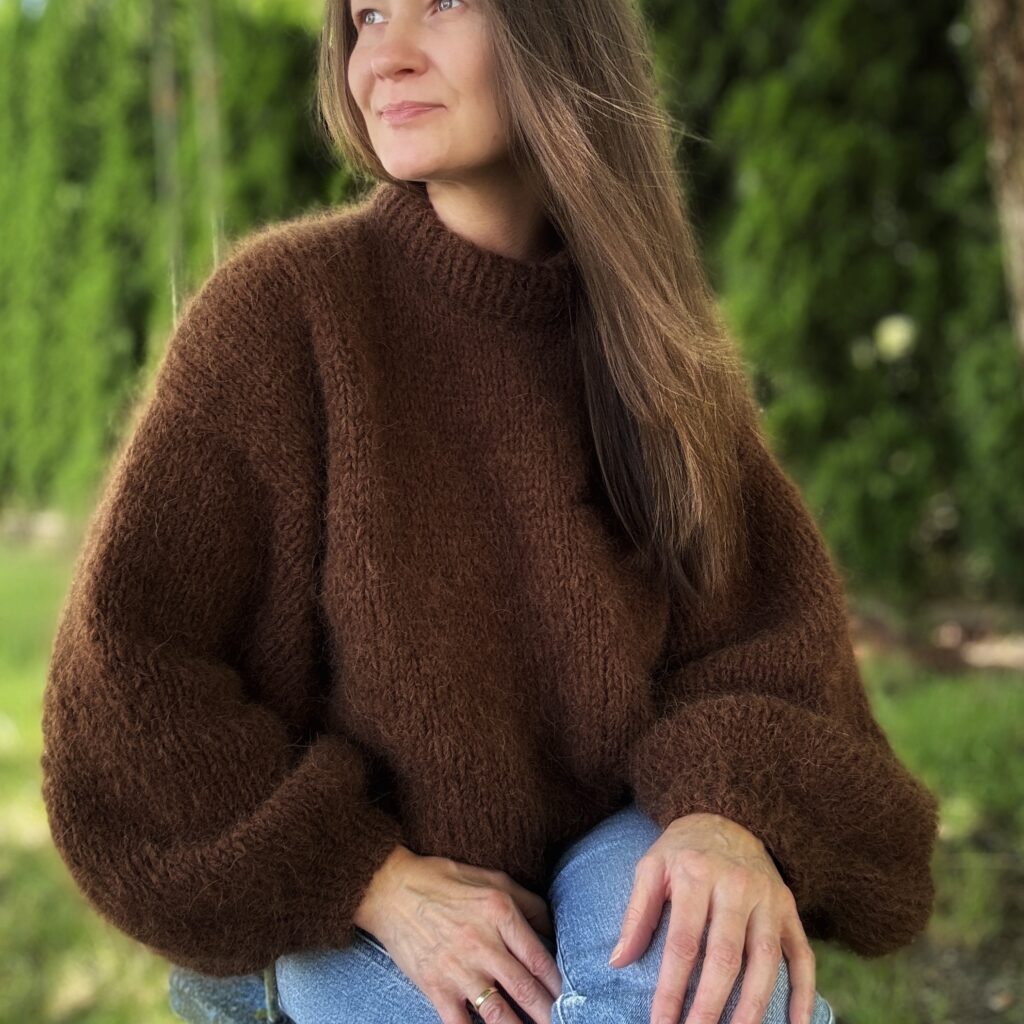Sweter z alpaki ręcznie dziergany w kolorze czekoladowym, pokazany na modelce w naturalnej scenerii.